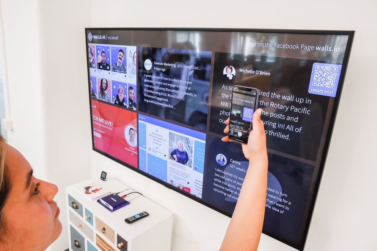 A woman uses a smartphone to scan a QR code on a digital wall display indoors.
