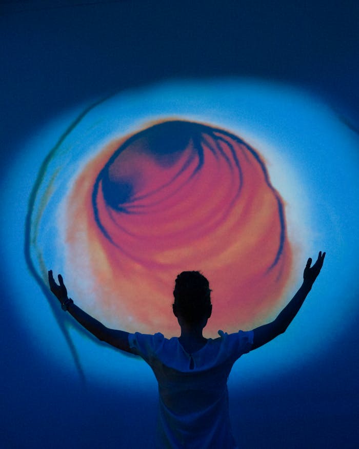 Person silhouetted against a vibrant abstract projection with swirling colors evokes wonder and mystery.